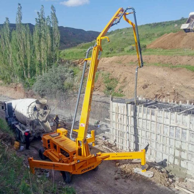 Bomba de hormigón Atabey Scorpion con la pluma desplegada vertiendo hormigón en un muro encofrado, junto a un camión mixer